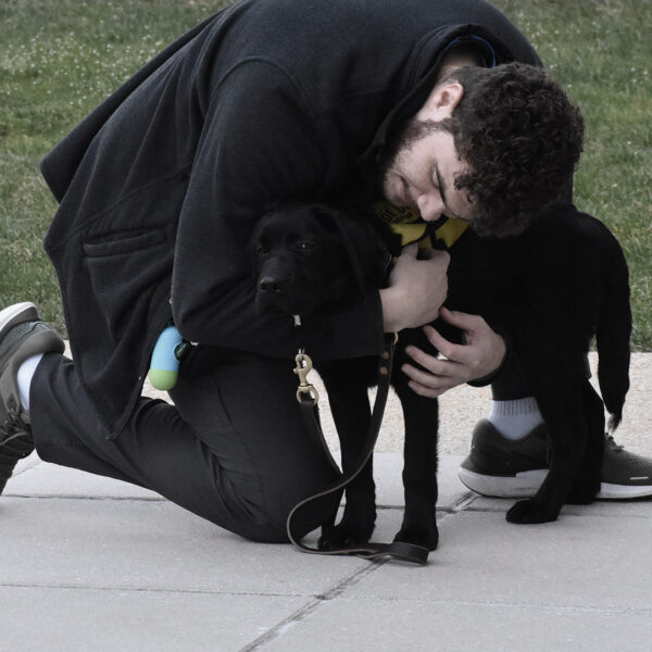 A guide dog handler trains with his future assistance dog by wrapping his arms around the puppy