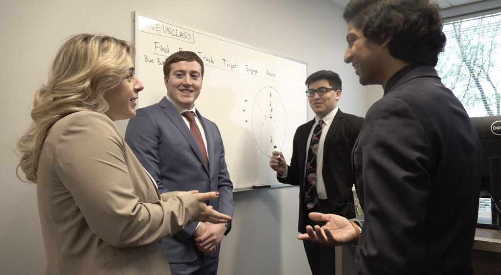 A group of four SPA employees smiling and dicussing around a whiteboard.