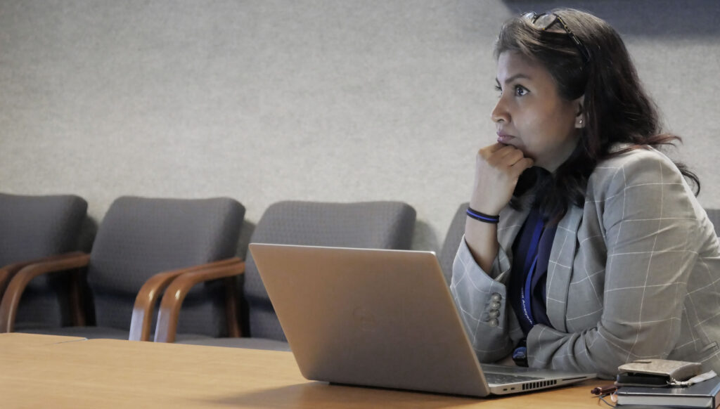 An SPA employee is at her laptop on a conference table during a meeting, listening to the speaker