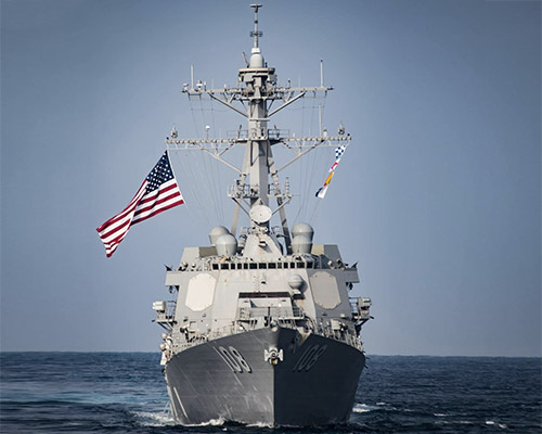 A straight on view of a large ship in water with an American flag waving in the wind