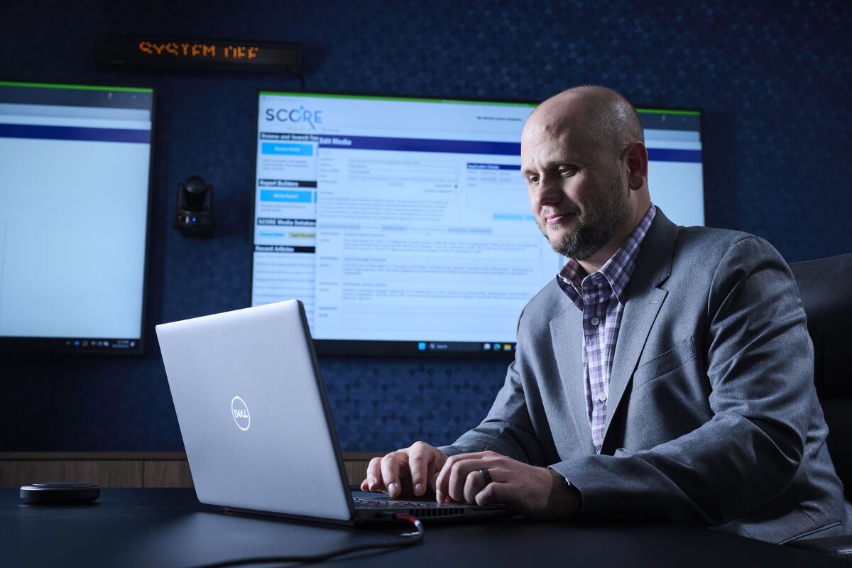 An SPA employee types on his laptop while presenting on large screens